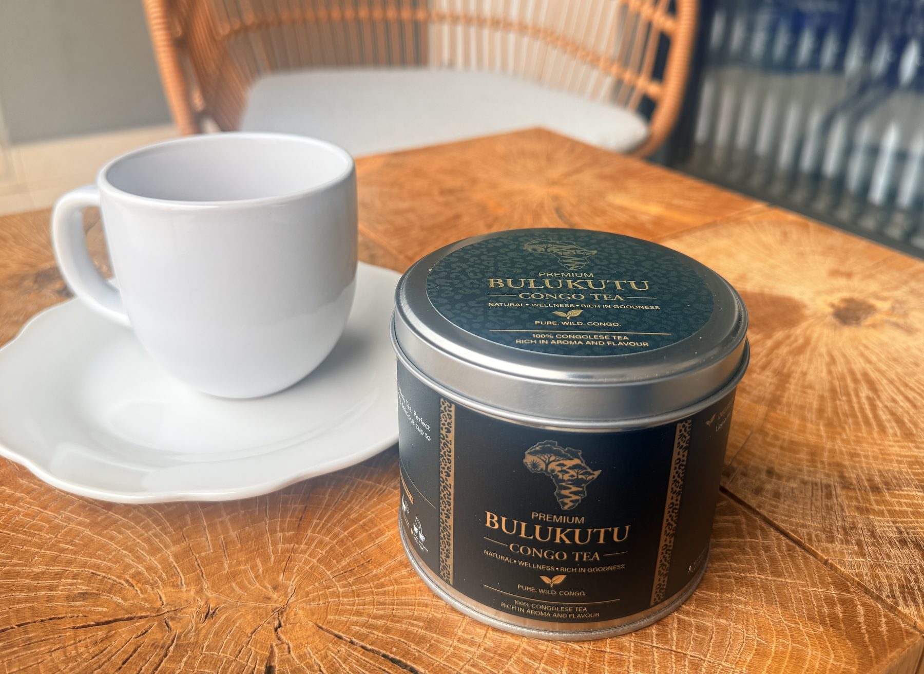 A tin of Bulukutu and an empty white cup on a cafรฉ table in the morning light